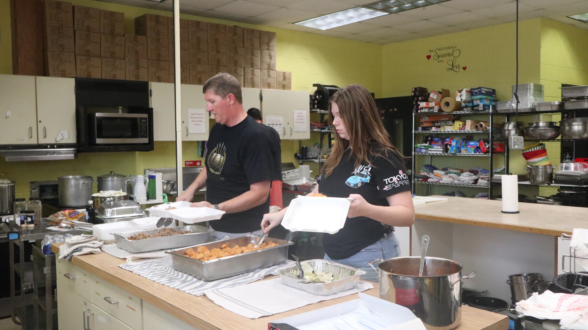 Two volunteers plating hot meals from serving pans during Team Mess Hall.